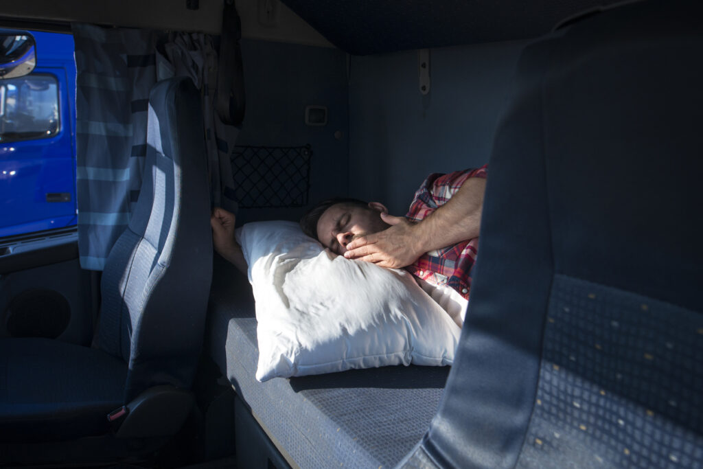 Truck driver yawning and waking up in his cabin at truck stop. Tired worker on his break resting due to long drive.