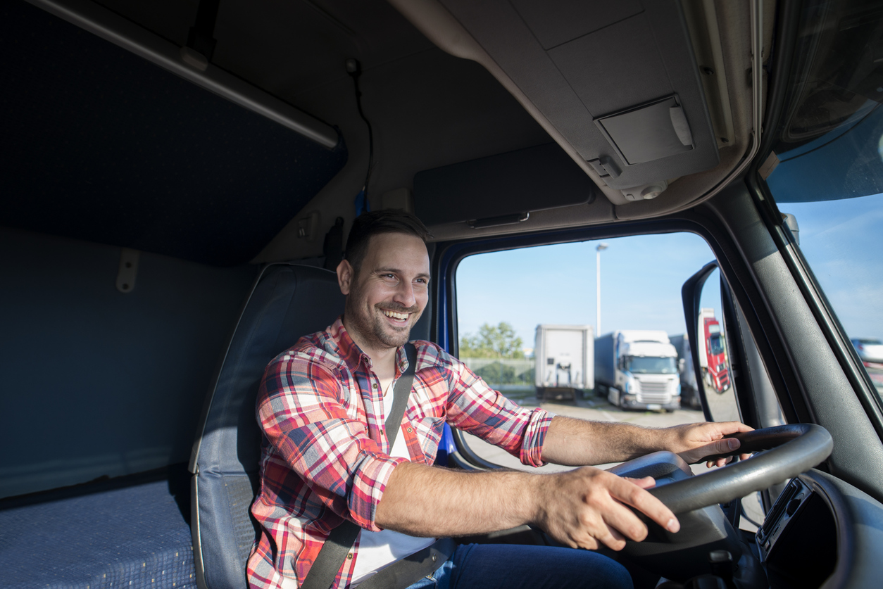 Shot of professional truck driver in casual clothing wearing seat belt on and driving his truck to destination. Smiling trucker enjoying his job. Transportation services.